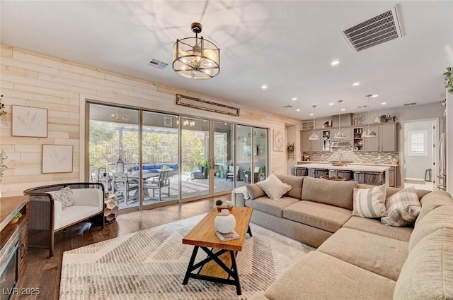 living area with recessed lighting, visible vents, wood walls, and wood finished floors