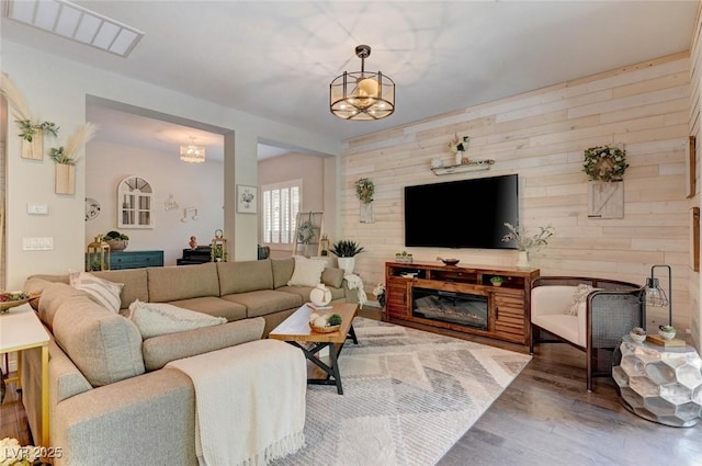 living area featuring a glass covered fireplace, visible vents, wooden walls, and wood finished floors