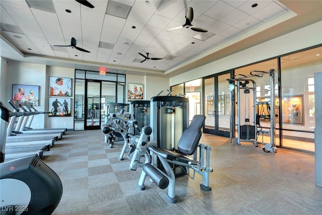 exercise room featuring a tray ceiling, french doors, carpet flooring, and a ceiling fan