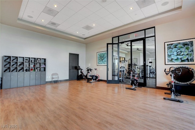 exercise room featuring wood finished floors, a raised ceiling, a high ceiling, and baseboards