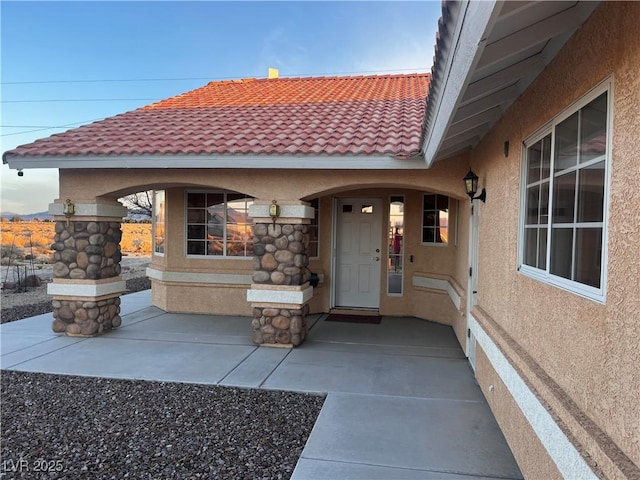 view of exterior entry with a tiled roof and stucco siding