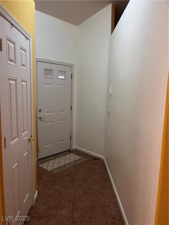 doorway with dark tile patterned flooring and baseboards