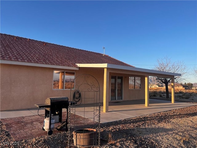 back of house featuring stucco siding, a tile roof, and a patio