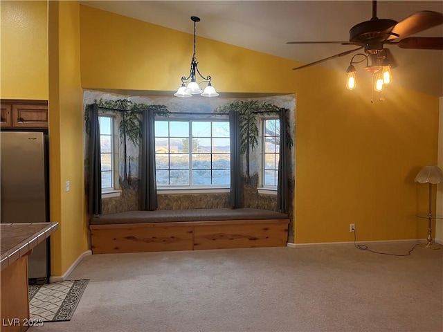 unfurnished dining area featuring light carpet, vaulted ceiling, baseboards, and ceiling fan with notable chandelier