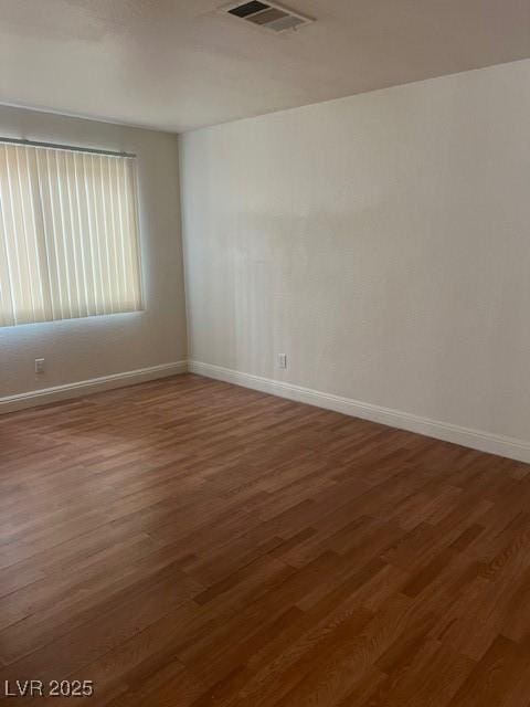 spare room featuring baseboards, visible vents, and wood finished floors