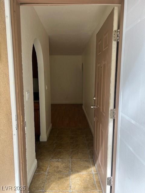 hall featuring stone finish floor, baseboards, and arched walkways