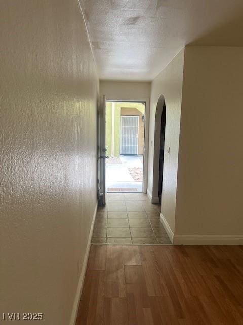 corridor with baseboards, a textured ceiling, arched walkways, and wood finished floors