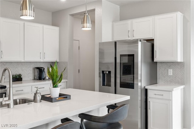 kitchen featuring a breakfast bar area, hanging light fixtures, light countertops, white cabinetry, and stainless steel refrigerator with ice dispenser