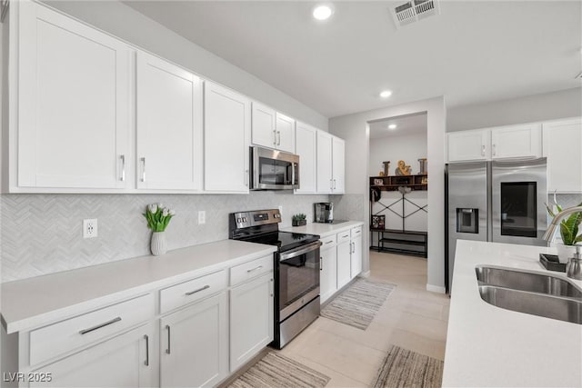 kitchen with visible vents, appliances with stainless steel finishes, a sink, white cabinetry, and backsplash