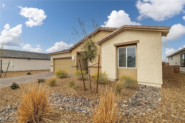 view of side of home featuring decorative driveway, an attached garage, and stucco siding