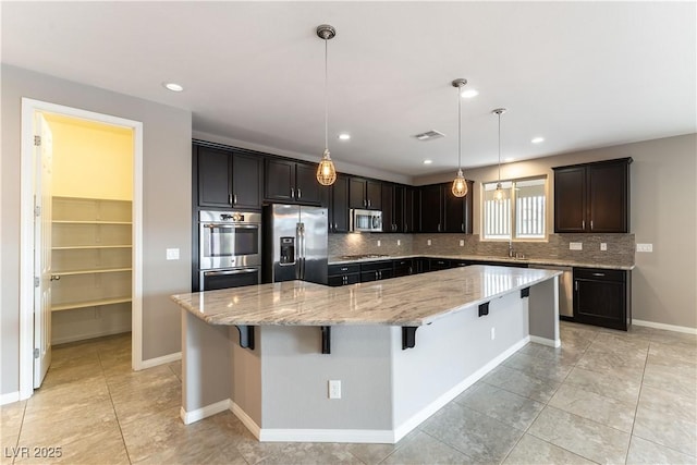 kitchen with stainless steel appliances, a sink, a large island, backsplash, and light stone countertops