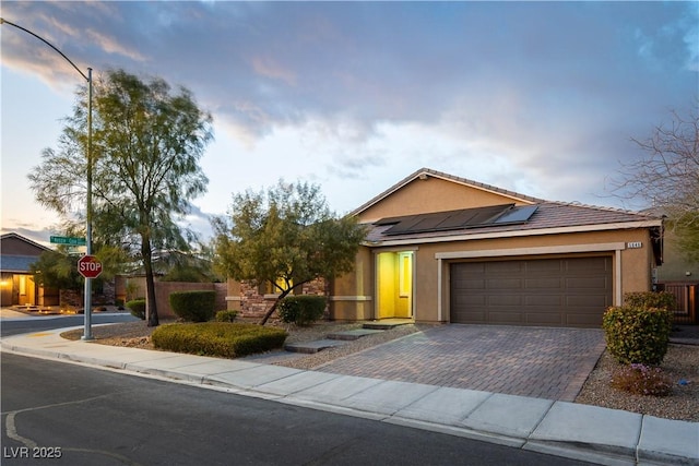 view of front of house with an attached garage, decorative driveway, solar panels, and stucco siding