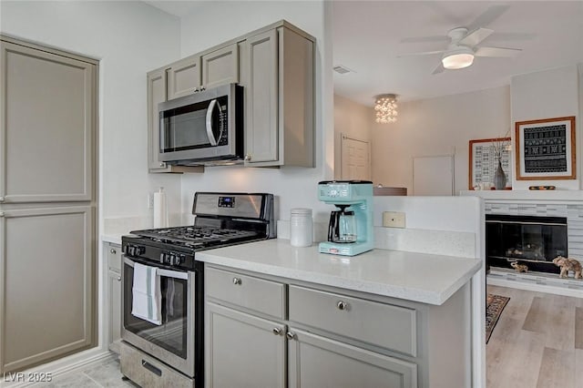 kitchen featuring stainless steel appliances, light countertops, gray cabinetry, light wood-style floors, and a glass covered fireplace