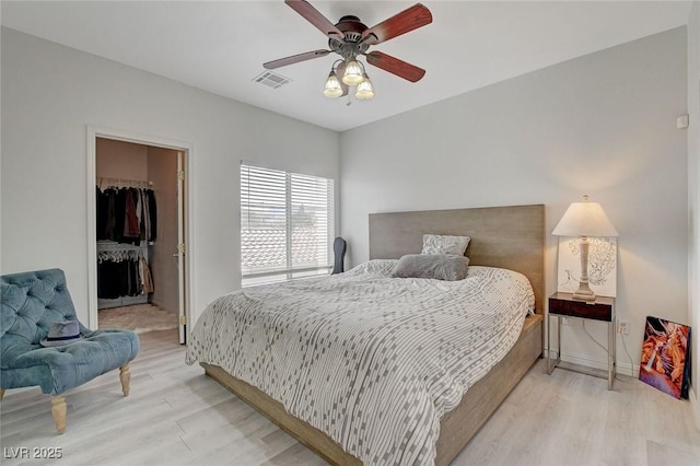 bedroom with a walk in closet, a closet, visible vents, a ceiling fan, and light wood-type flooring