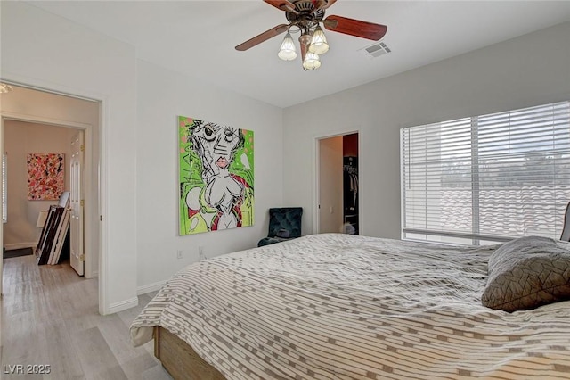 bedroom featuring visible vents, baseboards, ceiling fan, a spacious closet, and light wood-type flooring