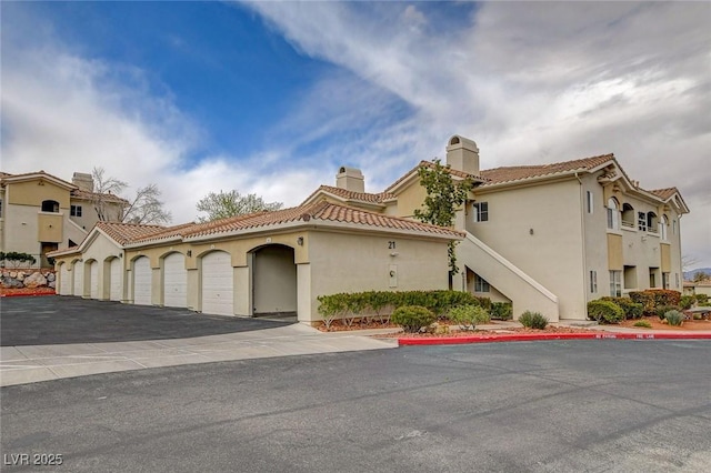 mediterranean / spanish-style house with a chimney, a tile roof, community garages, and stucco siding