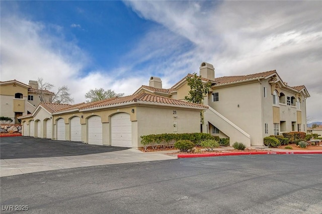 mediterranean / spanish house with stucco siding, a tiled roof, and community garages