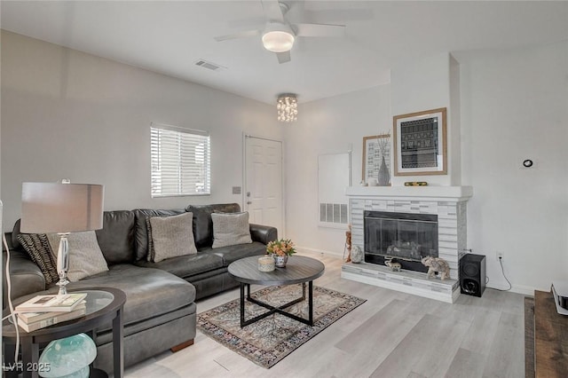 living room featuring a glass covered fireplace, visible vents, ceiling fan, and wood finished floors