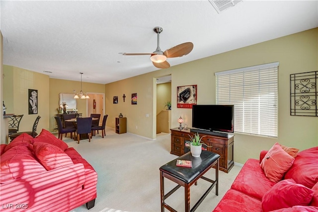 living area featuring light carpet, ceiling fan with notable chandelier, visible vents, and baseboards