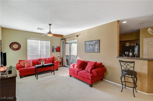 carpeted living area featuring a textured ceiling, baseboards, visible vents, and a ceiling fan