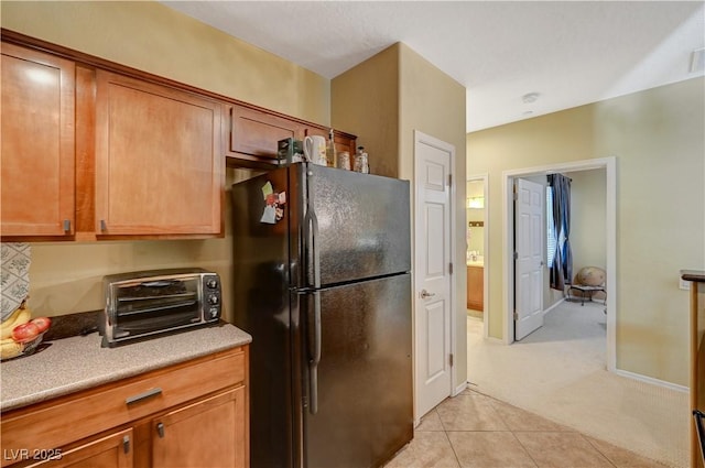 kitchen featuring light tile patterned floors, brown cabinetry, freestanding refrigerator, and a toaster