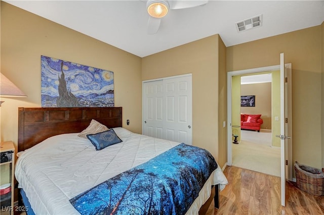 bedroom with a closet, wood finished floors, visible vents, and a ceiling fan