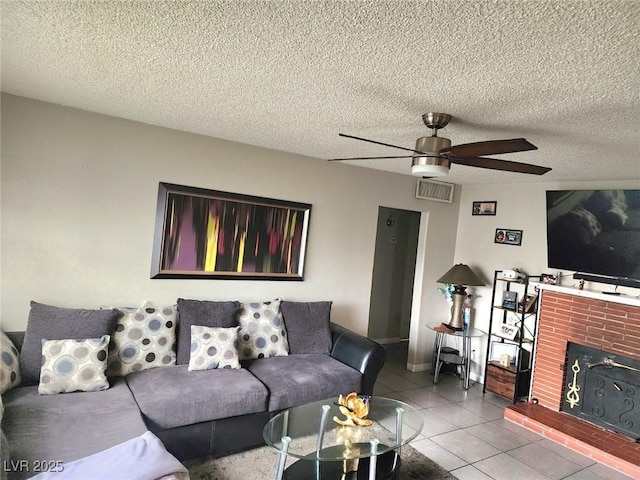 living area featuring light tile patterned floors, visible vents, ceiling fan, a textured ceiling, and a brick fireplace