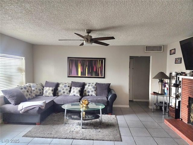 living area with light tile patterned floors, visible vents, ceiling fan, a textured ceiling, and a brick fireplace