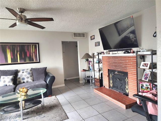 tiled living area with visible vents, a brick fireplace, ceiling fan, a textured ceiling, and baseboards