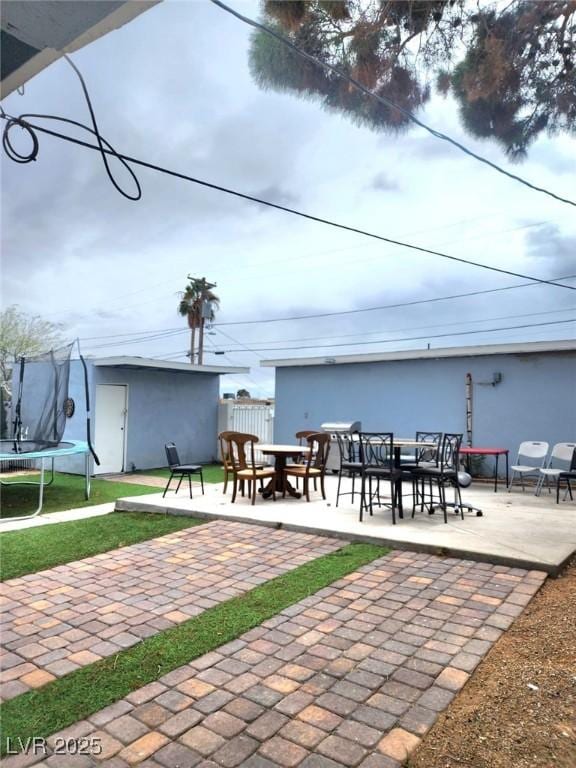 view of patio with a trampoline, an outdoor structure, and outdoor dining space