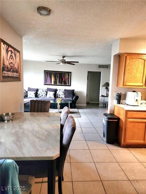 dining area with light tile patterned floors, ceiling fan, visible vents, and a textured ceiling