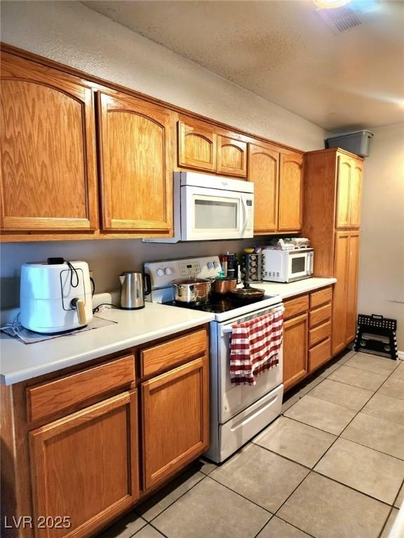 kitchen featuring white microwave, light tile patterned floors, light countertops, and electric stove