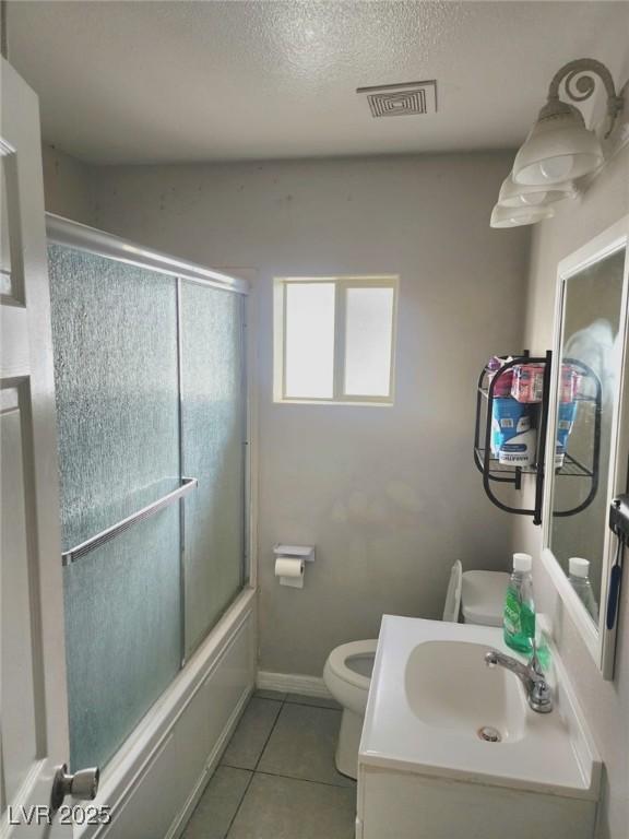 bathroom with bath / shower combo with glass door, visible vents, toilet, vanity, and tile patterned flooring