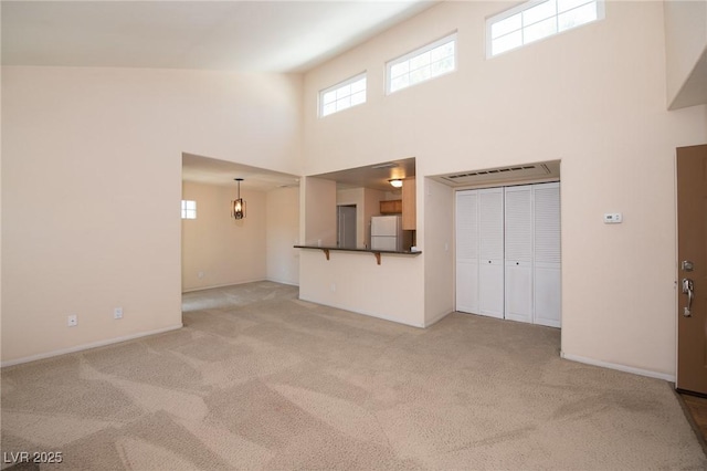 unfurnished living room featuring a towering ceiling, baseboards, and light colored carpet