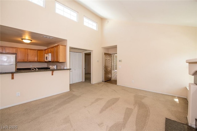 unfurnished living room with baseboards, a high ceiling, visible vents, and light colored carpet