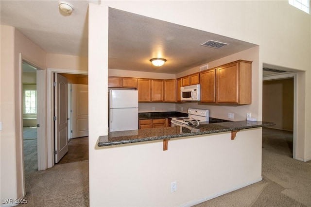 kitchen with white appliances, light colored carpet, visible vents, and a peninsula