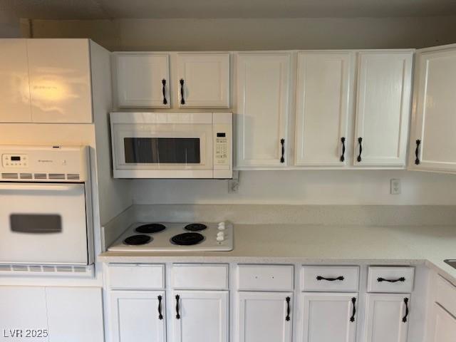 kitchen with white appliances, white cabinets, and light countertops