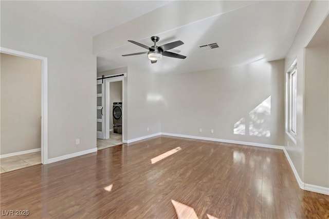 interior space featuring washer / dryer, a barn door, visible vents, ceiling fan, and wood finished floors