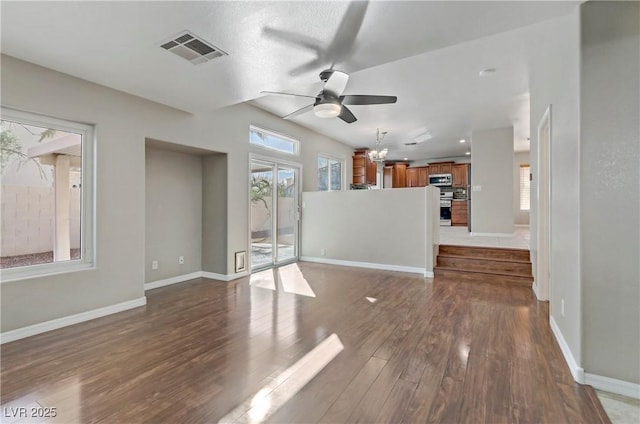 unfurnished living room featuring ceiling fan with notable chandelier, visible vents, baseboards, and wood finished floors