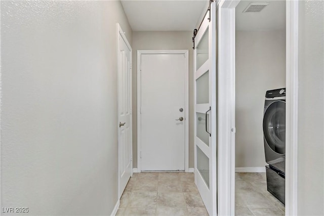 interior space featuring light tile patterned floors, a barn door, laundry area, visible vents, and baseboards