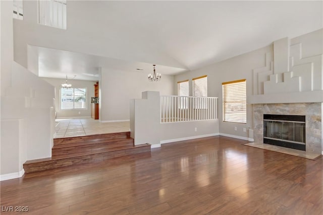 unfurnished living room featuring baseboards, wood finished floors, an inviting chandelier, vaulted ceiling, and a fireplace