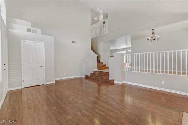 unfurnished living room with baseboards, visible vents, stairway, wood finished floors, and a chandelier