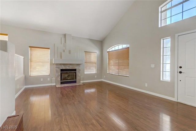 unfurnished living room featuring high vaulted ceiling, a tiled fireplace, baseboards, and wood finished floors