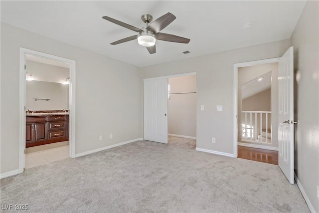 unfurnished bedroom featuring light carpet, a spacious closet, ensuite bath, and baseboards