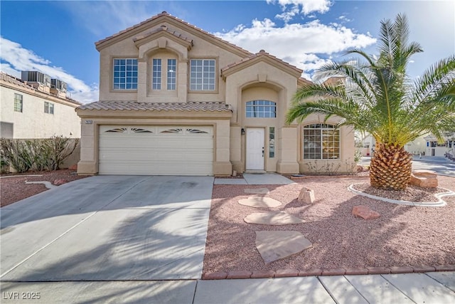 mediterranean / spanish house with a garage, a tiled roof, concrete driveway, and stucco siding