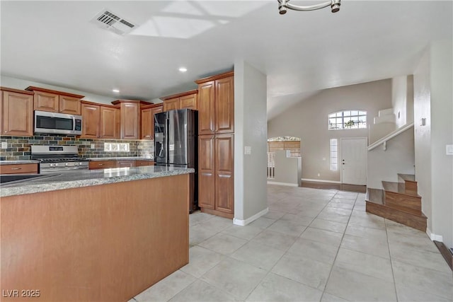 kitchen with brown cabinets, light tile patterned floors, stainless steel appliances, visible vents, and decorative backsplash