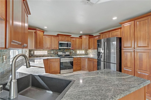 kitchen featuring stainless steel appliances, a sink, visible vents, backsplash, and light stone countertops