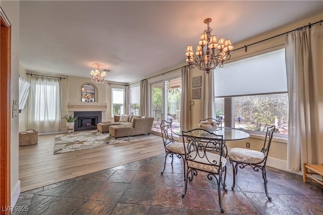 dining area with plenty of natural light, stone tile floors, a notable chandelier, and a lit fireplace