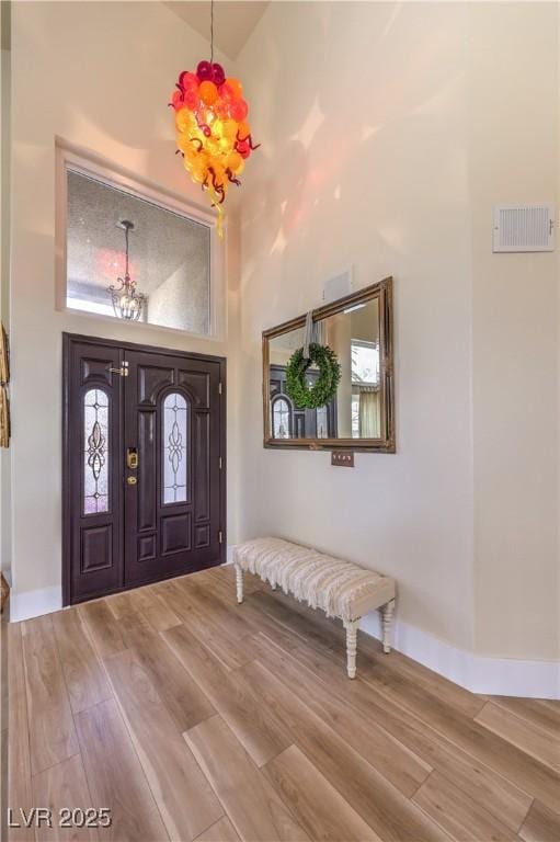 foyer entrance with high vaulted ceiling, wood finished floors, visible vents, and a notable chandelier