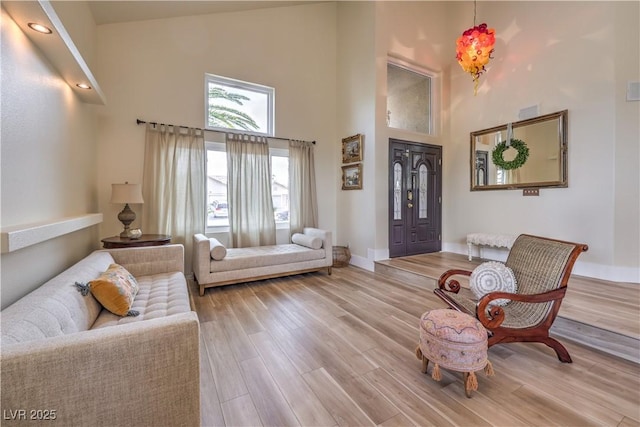 living area with light wood-type flooring, a high ceiling, and baseboards